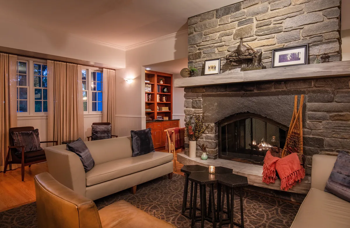 A cozy fireside sitting area featuring a decorative fireplace, comfortable seating, and a well-stocked bookshelf. Warm lighting enhances the inviting atmosphere, making it ideal for relaxing with a book or sharing quiet moments with friends and family.