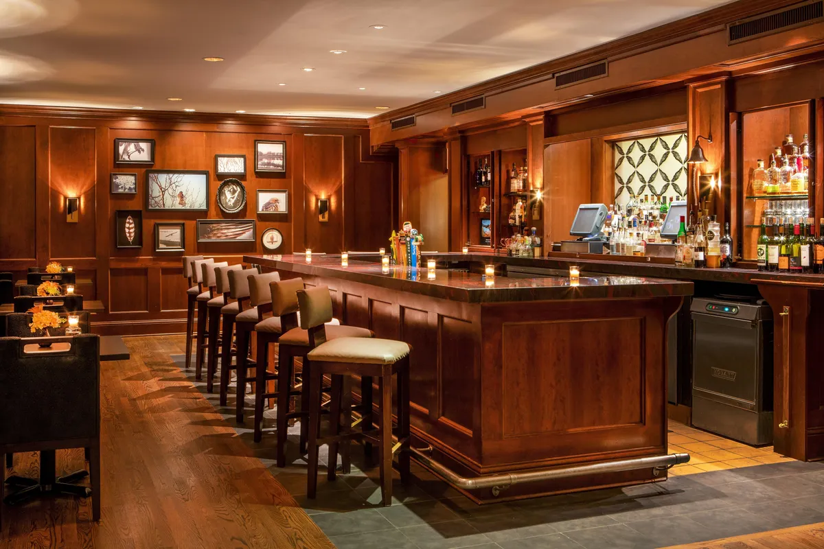 An elegant and relaxed interior scene featuring a well-stocked bar, cozy seating area, and tasteful wall art. Patrons are seen enjoying drinks, intimate conversations, and a sophisticated ambiance ideal for celebrating special moments.
