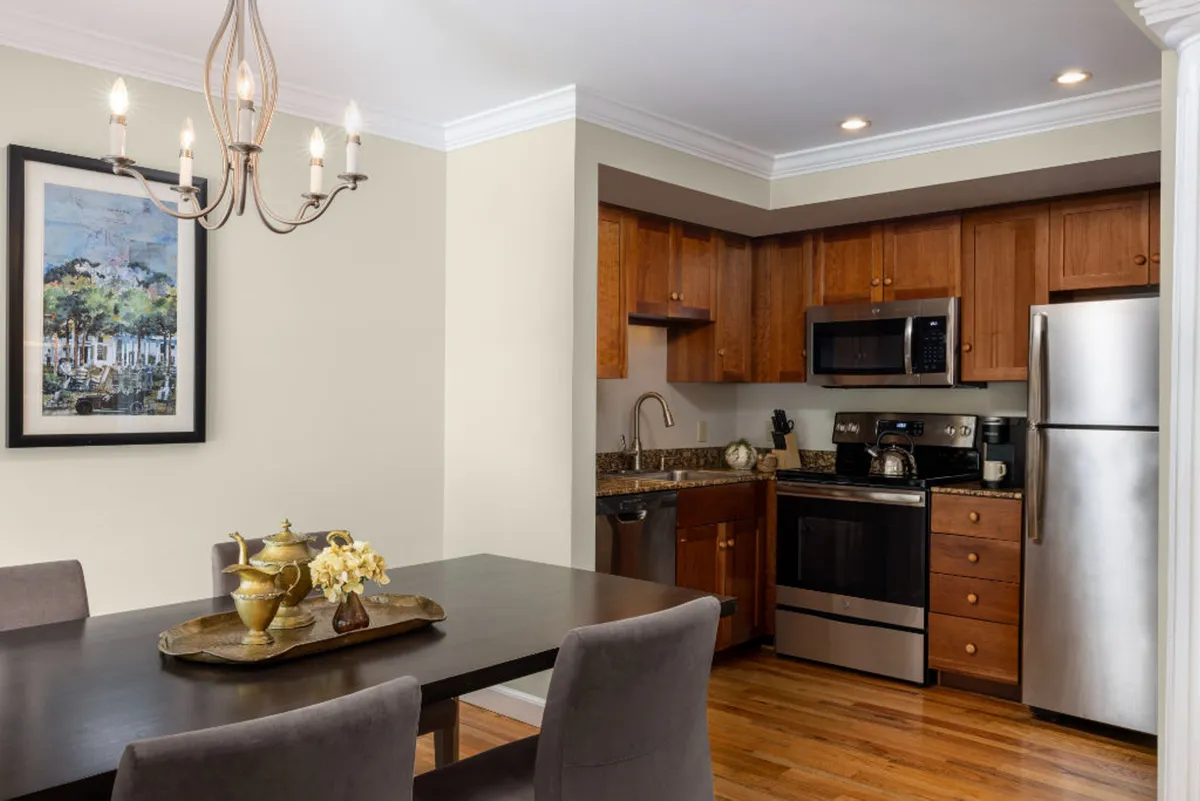 A cozy, well-appointed kitchen and dining area featuring a central dining table, modern kitchen appliances, a striking chandelier, and framed artwork on the walls. The warm lighting and inviting layout suggest a space ideal for family meals, cooking sessions, or entertaining guests.